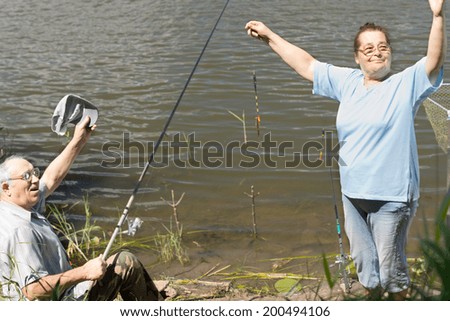 Fisherman celebrating the best catch of the day with his wife holding up a tiny tiddler in the hook with a theatrical flourish in a fun gesture