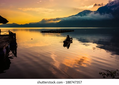 A Fisherman Fishes In A Traditional Paddle Boat In The Morning Before Sunrise On This Volcano Crater Lake In Bali, Indonesia.