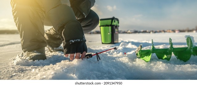 Fisherman is fishing in a hole on a large frozen lake on a sunny day. The joy of winter fishing. - Powered by Shutterstock