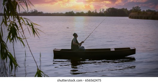 fisherman fishing on bank of river at sunset in boat