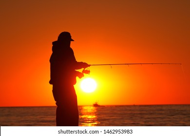 Fisherman fishing on pier in the morning with sunrise and passing boat in the background. - Powered by Shutterstock