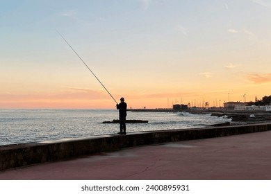 Fisherman with fishing rod on the pier at sunset, Oeiras, Portugal  - Powered by Shutterstock