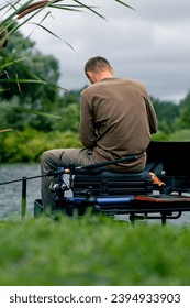 Fisherman with fishing rod or spinning and professional tools sitting on the river bank rear view Pull fish out of lake sports fishing - Shutterstock ID 2394933903