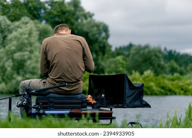 Fisherman with fishing rod or spinning and professional tools sitting on the river bank rear view Pull fish out of lake sports fishing - Shutterstock ID 2394933905