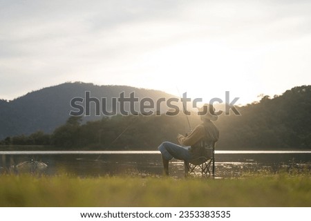 Fisherman man fishing with a spinning fishing rod in hand, close-up on the bank of a river or lake. With the light scene during the sunset against the natural forest in the background Hobby,fisherman.