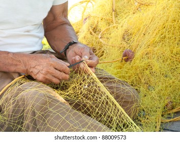 A fisherman mending his yellow fishing net on his boat in Greece.