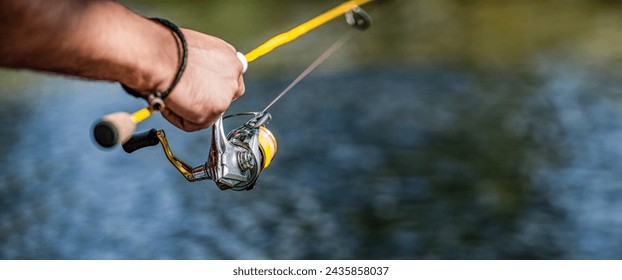 Pescador en la orilla del río. Hombre pescador atrapa un pez. Pescador en su mano sosteniendo el giro. Mano del pescador que sostiene la caña de pescar con el carrete. Carrete de pesca. Caña de pescar con carrete de aluminio.