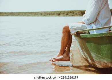 Fisherman relaxing on sunny day, cooling barefoot legs in lake water. Cut out image of unrecognizable male  sitting on the boat. Summer Holiday background. Copy space