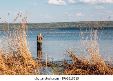 A Fisherman In A Rubber Bib Overalls Fishing On The Lake