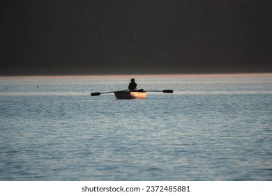 A fisherman sailing by boat at dawn on the lake - Powered by Shutterstock