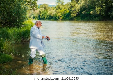 Fisherman senior rich businessman in suit caught a fish. Man fishing on river.