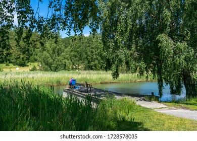 A Fisherman Sits On A Wooden Pier On The Lake. Pensioner Senior Is Fishing During The Epidemic Of The Covid 19 Coronavirus. No Quarantine Or Self-isolation.