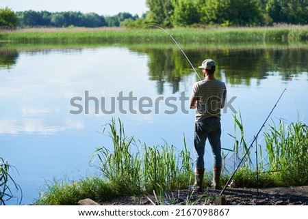 Fisherman standing in the side of the river during sunset and catching a fish with spinnings. Adult lifestyle.