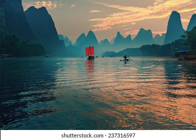 Fisherman stands on traditional bamboo boats at sunrise (boat with a red sail in the background) - The Li River, Xingping, China - Powered by Shutterstock