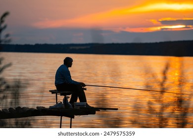 Fisherman at Sunset. A silhouette of a man fishing on a dock at sunset. The sky is ablaze with orange and yellow hues, reflecting on the still water. - Powered by Shutterstock