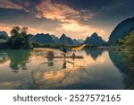 Fisherman with traditional fishing on wooden raft on the lake in the sunset, surrounded by mountain in Phong Nam Valley, Cao Bang, Vietnam