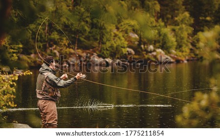 Fisherman using rod fly fishing in mountain river autumn splashing water.