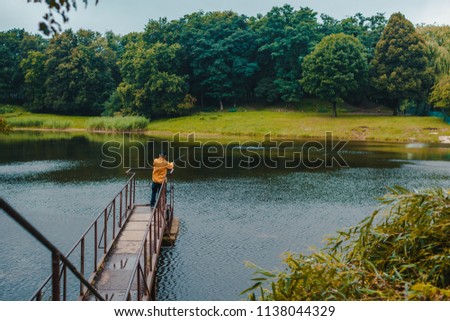 Fisherman in yellow jacket standing on pier of the lake and fishing on rainy day