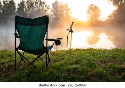 Fisherman's chair and fishing rods in the background over the lake at sunrise, foggy morning. Fishing concept. Beautiful sunrise - morning landscape. Place of a fisherman with fishing rod into the fog