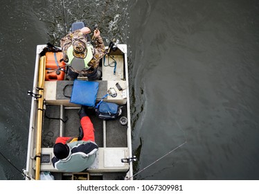 Fishermen In A Fishing Boat With Tackle Box, Fishing Rods, And Gear. Above View From A Drone Of A Man Casting His Bait And Reeling In A Fish.
