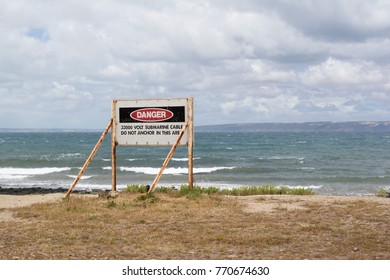 Fishery Beach, South Australia, Australia - December 2, 2017: Danger signage on the beach  indicating a 33000 Volt Submarine cable, Do not anchor in this area. Kangaroo Island seen in distance.