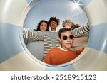 Fisheye shot of four teenagers posing together for camera holding swimming tube while enjoying sunshine on beach, camera flash, copy space