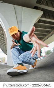 Fisheye of young Asian man dancing outdoors and gesturing to camera wearing colorful street style clothes