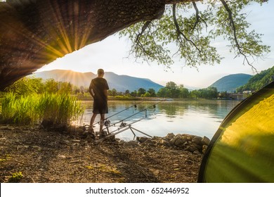 Fishing adventures, carp fishing. Angler, at sunset, is fishing with carpfishing technique. Camping on the shore of the lake. Fisherman in backlight