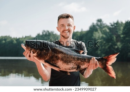 Fishing backgrounds. Happy fisherman hold big trophy fish near lake. Success pike fishing. Big fresh fish trophy in hands. Young man returning with a freshly caught fish. Article about fishing day.