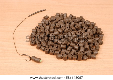 Fishing bait with hook and brown pre-drilled halibut pellets for carp fishing isolated on wood background with soft shadow
