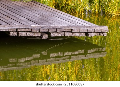 Fishing bench, wooden pier, dock on the shore of a calm pond or lake in summer with reflecting in the water - Powered by Shutterstock