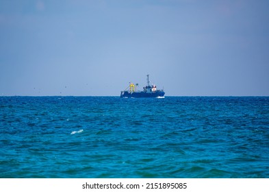 Fishing boat in blue sea and clear sky with birds flying overhead. Calm blue sea with the silhouette of a ship on the horizon