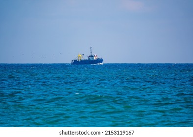 Fishing boat in blue sea and clear sky with birds flying overhead. Calm blue sea with the silhouette of a ship on the horizon