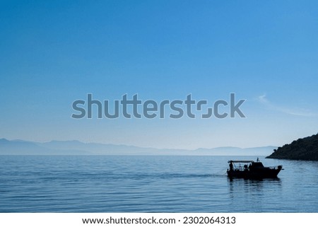 fishing boat silhouette on sea with misty mountains in the background