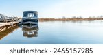 Fishing boats moored at wooden pontoon pier in early morning. Modern motorboats in small docks on calm river. Wide angle shot