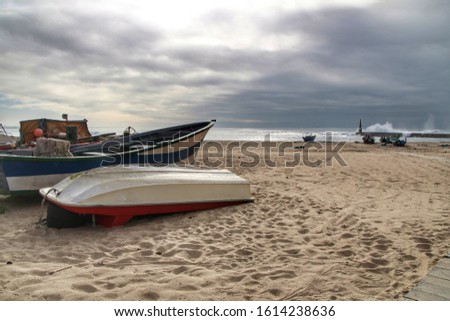 Fishing boats stranded on Aguda beach and Giant waves breaking on the breakwater and the lighthouse on Aguda Beach