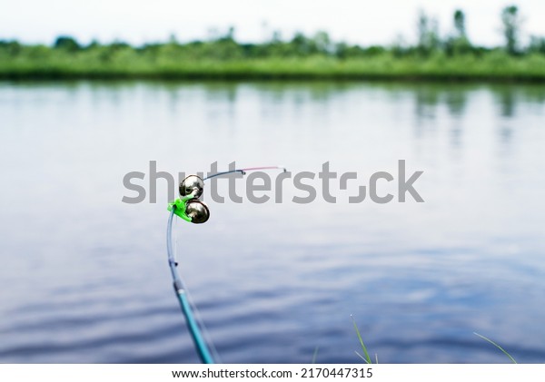 Fishing bottom tackle\
feeder with a signaling bell on the river bank on a summer day,\
soft selective focus