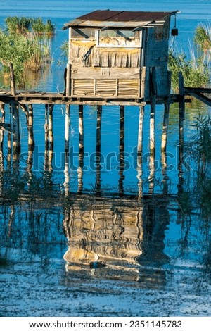 Fishing cabin hut. Wooden pillars in the water. Reflection from the sun.  Green reeds. Dojran lake, 2023 Macedonia.  Symmetry concept.