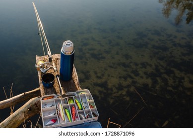 Fishing Day. Fishing Tackle - Fishing Spinning, Rod, Reel, Hooks, Fly, Bait, Lures In Box On Wooden Pier On Pond Background. Top View. Fishing For Pike, Perch. Recreation. Vintage Banner For Design.