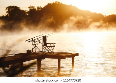 Fishing equipment on seat on lake. Feeder carp rods on wooden pier.