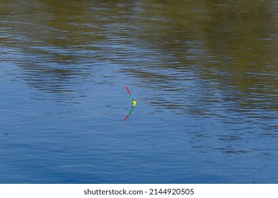 Fishing Float In The Blue Water. A Bobber Floats On The Water Surface Of The Lake Making Circles In The Water. 