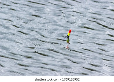 Fishing Float (bobber) Against The Background Of Water Close-up. Small Waves And Reflections Of The Sun On The Surface Of The Water. Fishing Concept And Place For Text.