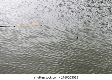 Fishing Float (bobber) Against The Background Of Water Close-up. Small Waves And Reflections Of The Sun On The Surface Of The Water. Fishing Concept And Place For Text.