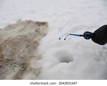Fishing in a frozen lake after drilling a hole in the ice. Reindeer skin in the snow