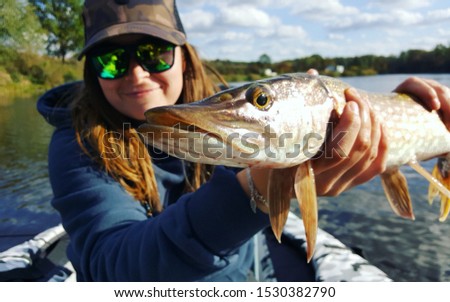 Fishing. Happy smiling fisher woman and trophy Pike, autumn colours and a beautiful lake
