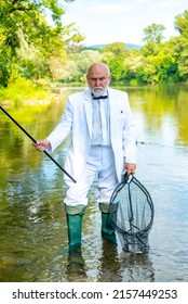 Fishing hobby and summer weekend. Portrait of senior businessman fishing. Mature man fisherman in white suit and bowtie with fishing rod, spinning reel on river.