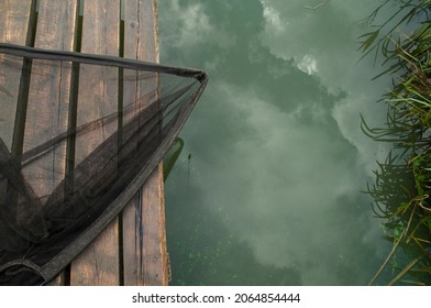 Fishing Landing Net On The Wooden Bridge. Reflecting Sky On The Water