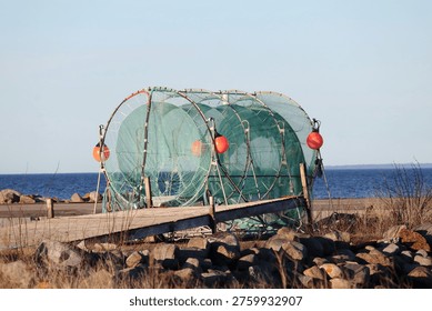 Fishing net frames standing by the sea on a sunny coastal day with rocks, blue water and clear open sky.