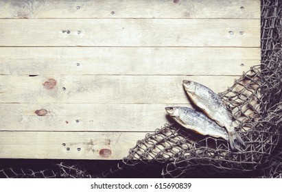 Fischernetze und getrockneter Fisch auf Holzhintergrund.