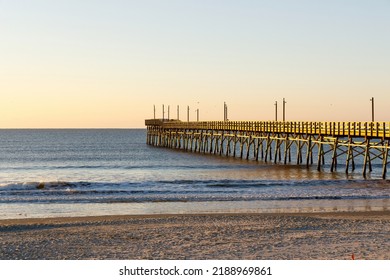 Fishing Pier On The Atlantic Ocean, Sunset Beach, North Carolina At Sunrise With A Clear Blue Sky